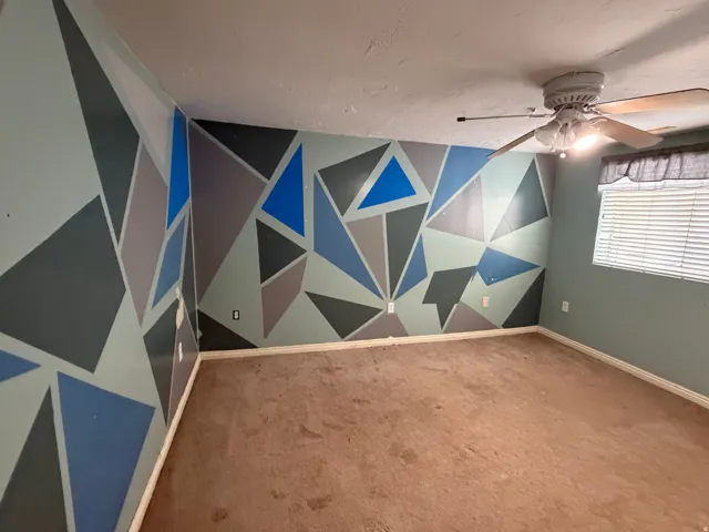 Room featuring patterned accent walls, carpet flooring, a ceiling fan with integrated lighting, and a window with horizontal blinds