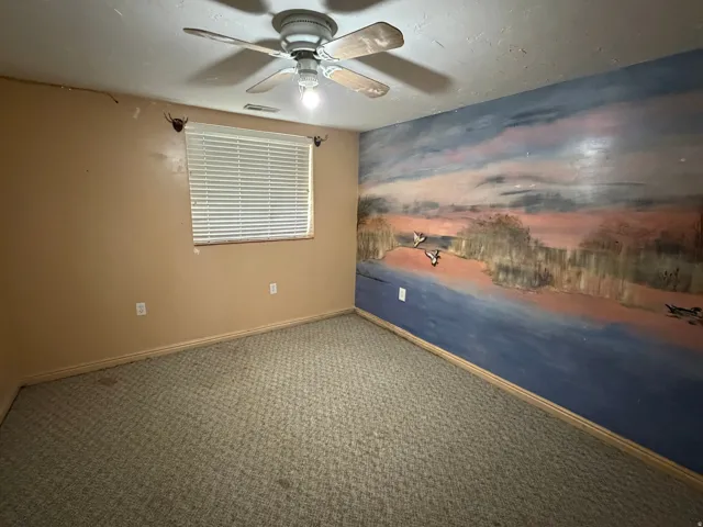 Room featuring a decorative mural wall, neutral tone carpet, and a ceiling fan with integrated lighting