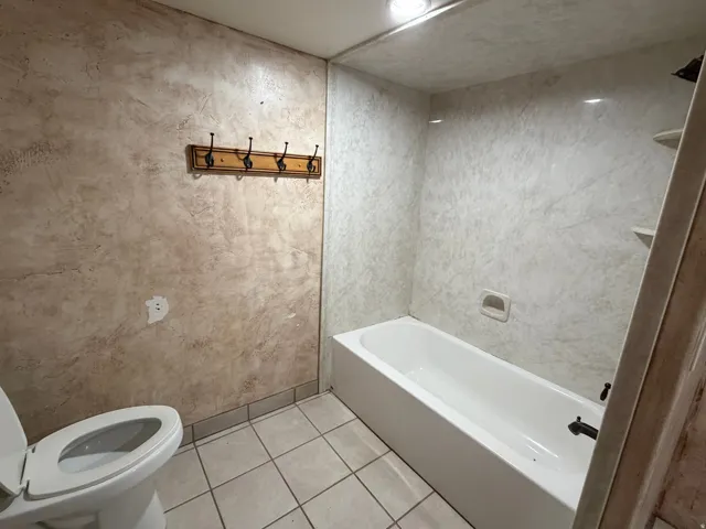 Bathroom featuring a full bathtub with light-toned wall panels, a wall-mounted coat rack, and recessed ceiling lighting