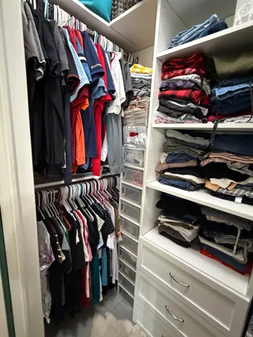 Master Walk-in closet featuring white built-in shelving, multiple hanging rods, integrated drawers with curved silver-tone pulls, and additional clear storage bins