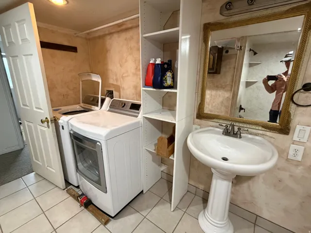 Dedicated laundry space featuring a white washer and dryer, adjacent to a pedestal sink with a framed mirror