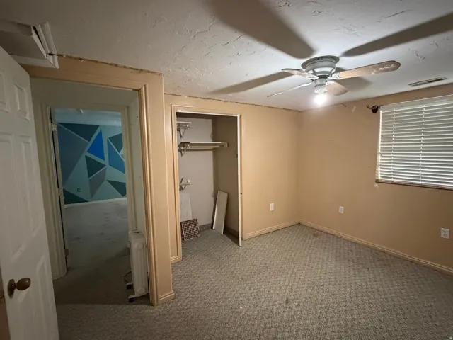Room with textured beige walls, patterned carpet, and a ceiling fan with light fixture