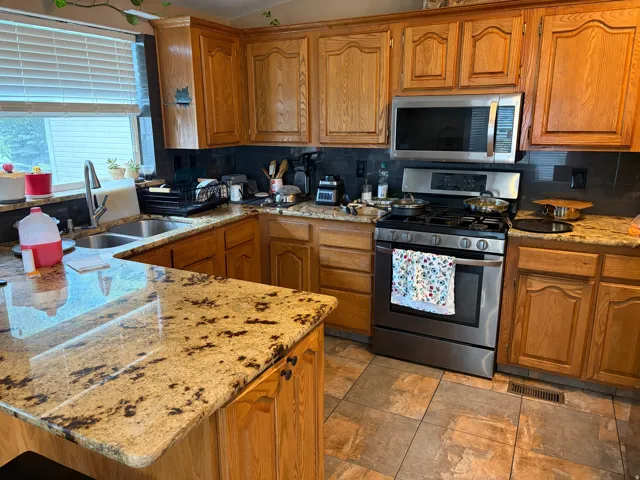 Kitchen featuring wood cabinetry, granite-finish countertops, stainless steel appliances, a double basin sink with a high-arc faucet, Tile backsplash