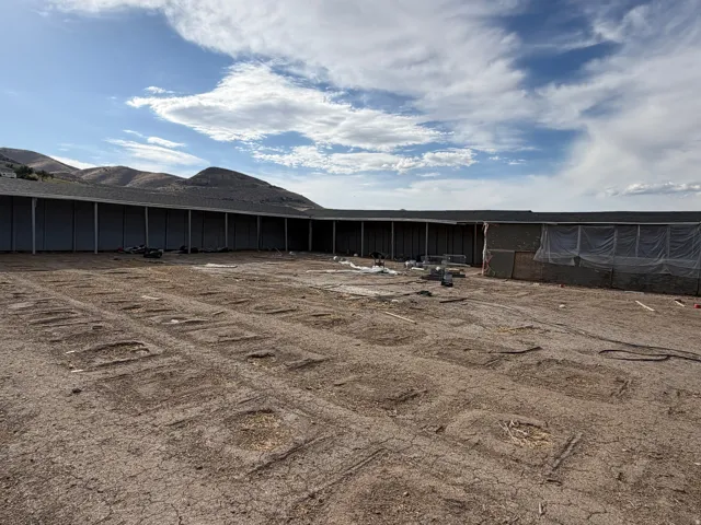 Expansive level lot with a structure featuring a dark shingled roof and light-colored siding, set against a backdrop of distant hills