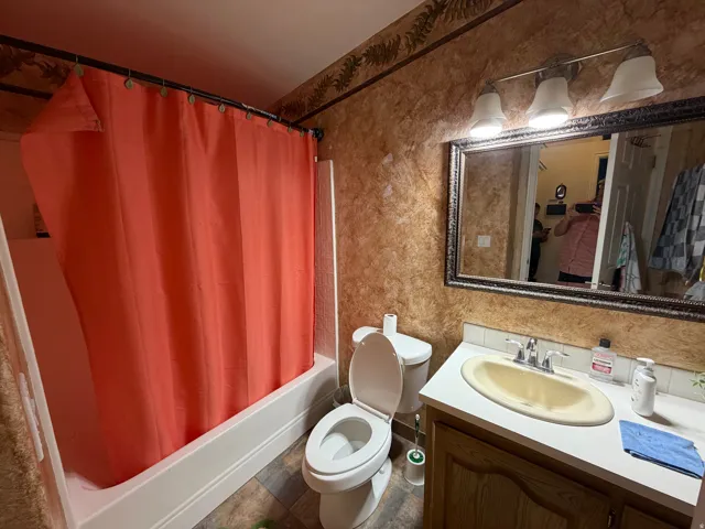 Mainlevel Bathroom featuring a single vanity with an integrated sink, framed wall mirror, and a three-light fixture, Vaulted ceiling