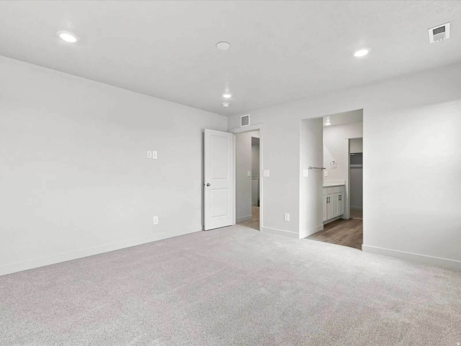 Recessed lighting, light gray carpeting, crisp white walls, white interior doors, and wood-finish flooring in an adjacent area