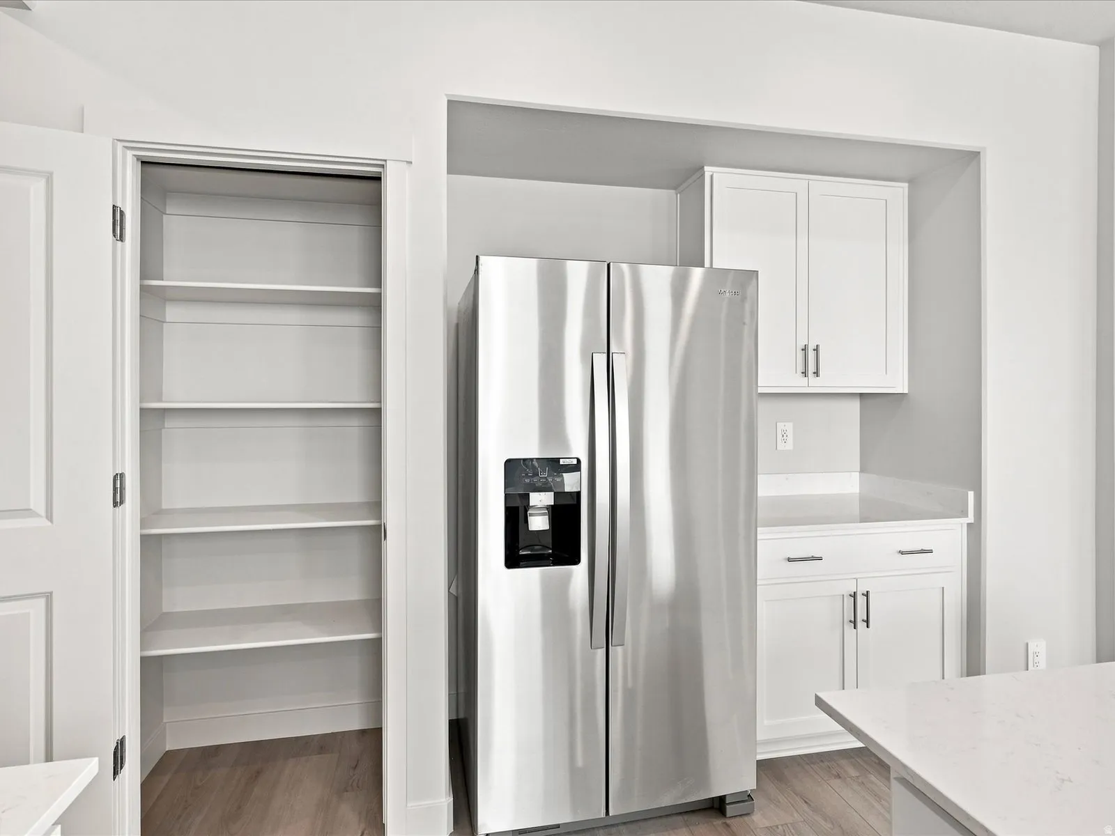 Built-in pantry shelving, stainless steel side-by-side refrigerator, white cabinetry, integrated countertop, and wood-finish flooring