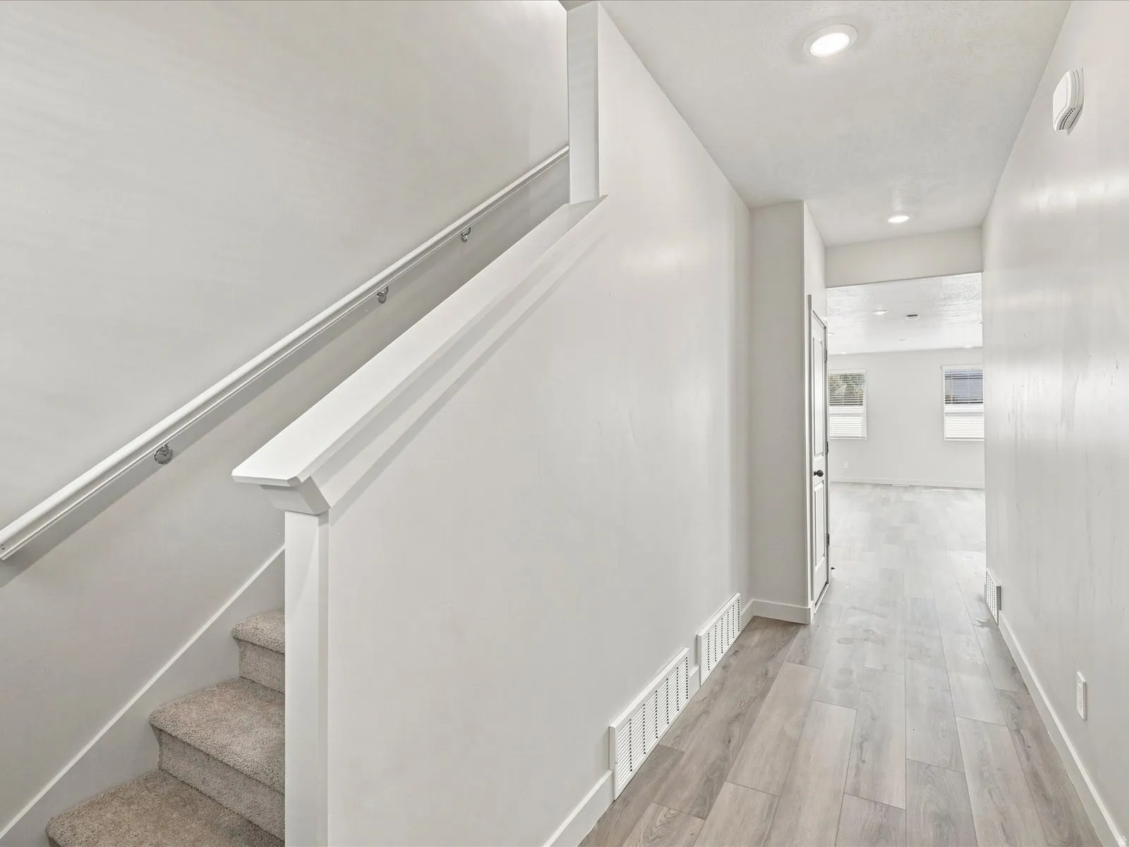 Carpeted staircase with white handrail and newel post, wood-finish flooring, recessed lighting, and white walls