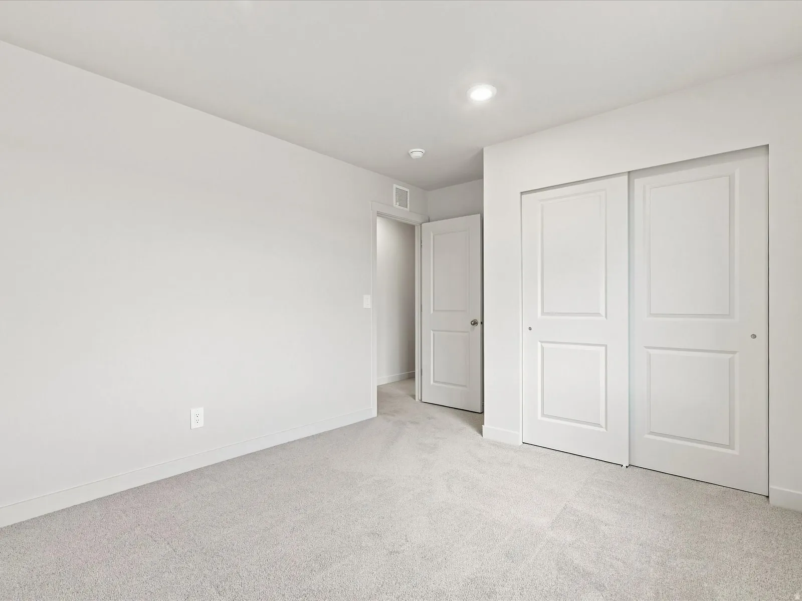 Light gray wall-to-wall carpeting, recessed ceiling lighting, a door with a polished chrome knob, and white sliding closet doors