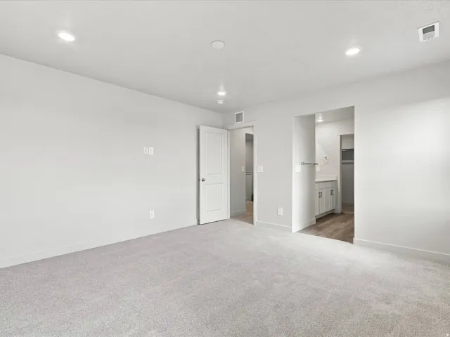 Recessed lighting, light gray carpeting, crisp white walls, white interior doors, and wood-finish flooring in an adjacent area