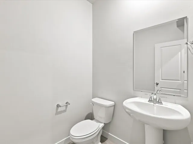 Pedestal sink with chrome faucet, wall-mounted mirror, and white toilet