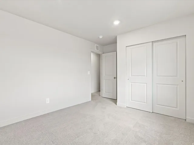 Light gray wall-to-wall carpeting, recessed ceiling lighting, a door with a polished chrome knob, and white sliding closet doors