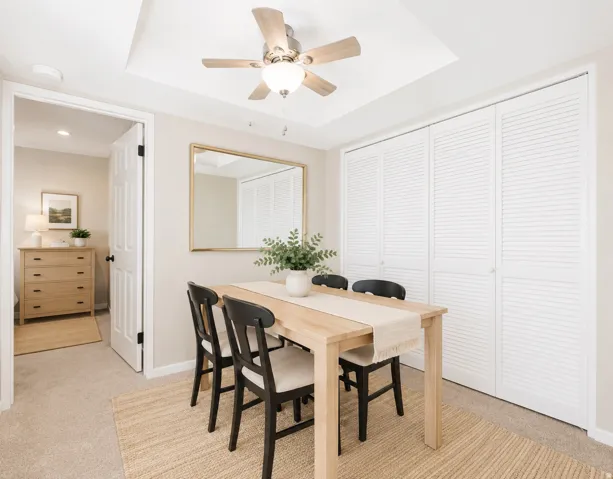 Tray ceiling with a ceiling fan light fixture, louvered bi-fold closet doors, and neutral wall paint