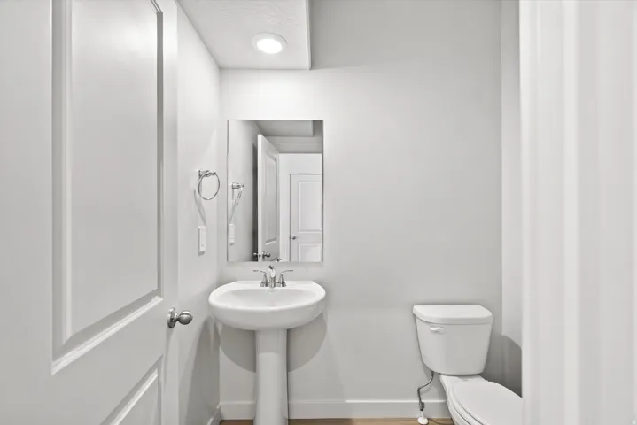 Pedestal sink with chrome faucet, wall-mounted mirror, and recessed lighting