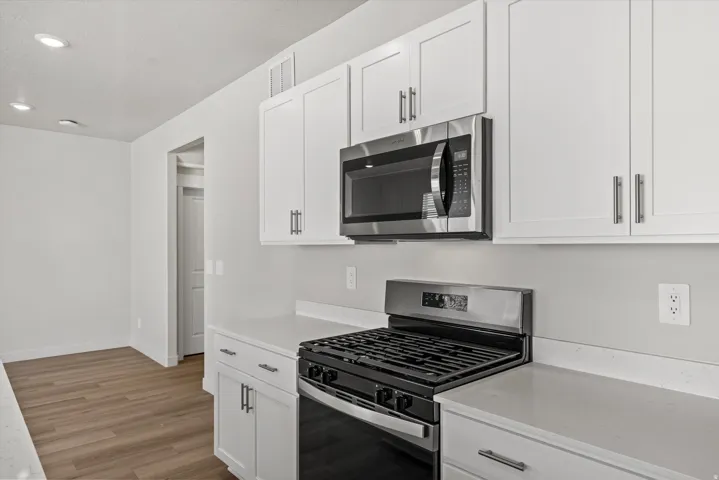 Modern kitchen featuring white shaker cabinetry, stainless steel appliances including a gas range and microwave, light-toned countertops, and wood-finish flooring