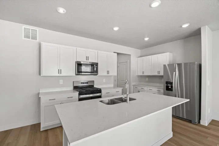 Contemporary kitchen featuring white cabinetry, a stainless steel appliance package, a center island with a double basin sink, recessed lighting, and wood-finish flooring