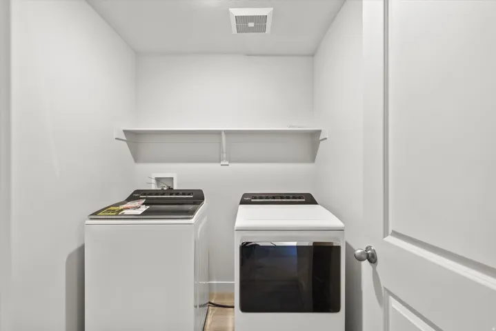 Dedicated laundry space featuring a floating shelf, light wood-finish flooring, and a ceiling-mounted ventilation fan