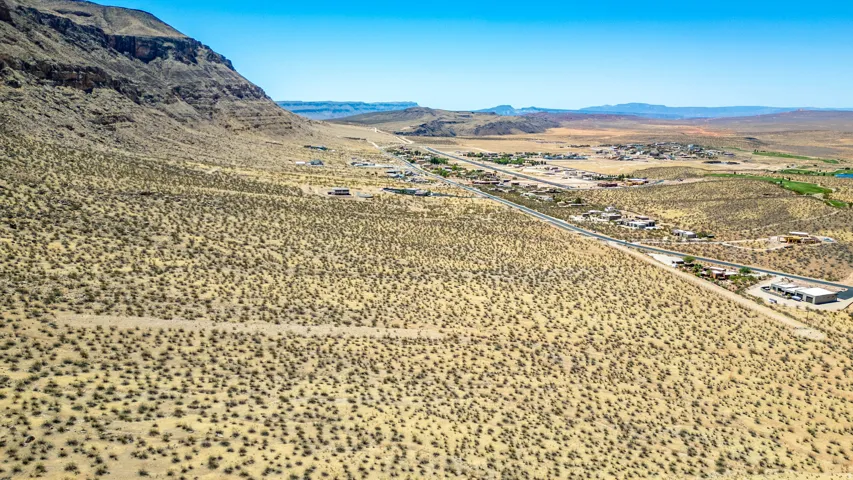 Expansive desert landscape featuring a paved road, scattered structures, and distant mountains under a clear sky