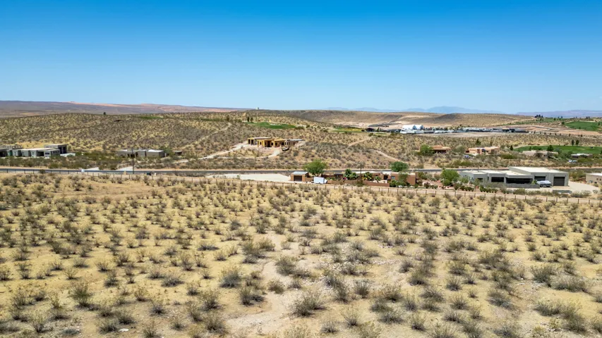 Expansive desert landscape featuring scattered brush and distant structures under a clear sky