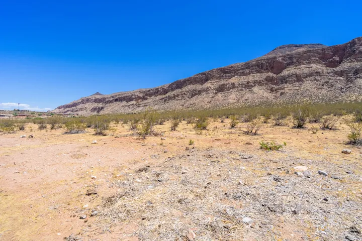 Expansive desert landscape featuring rugged mountain formations, natural scrub brush, and distant structures