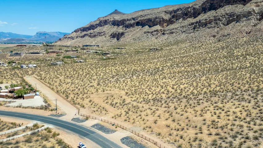 Desert landscape featuring a paved roadway, undeveloped land, and distant residential structures