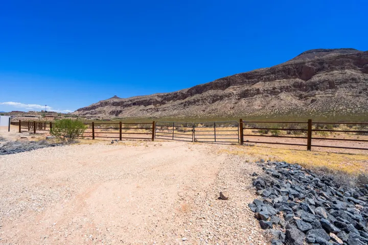 Gravel drive with metal fencing and gate, framed by a rock-lined embankment