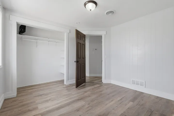 Spacious room featuring wood-finish flooring, white paneled walls, and a recessed closet with shelving