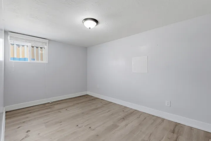 Room featuring light wood-finish flooring, white baseboards, a window with horizontal blinds, and a ceiling-mounted light fixture