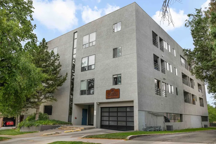 Contemporary multi-story building featuring a textured facade, floor-to-ceiling windows, private balconies with metal railings, and an integrated garage with a modern glass-paneled door
