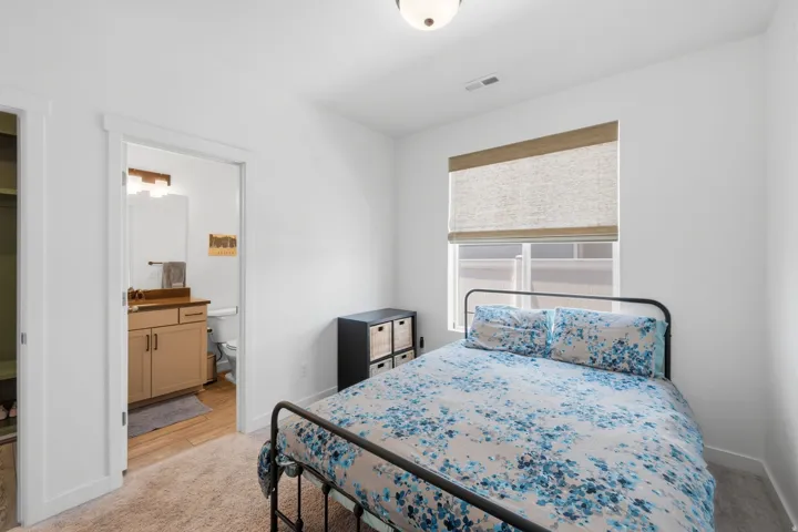 Bedroom featuring neutral carpeting, white walls, and a window with a woven Roman shade
