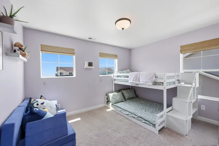 Carpeted room featuring multiple windows with natural light, a ceiling-mounted light fixture, and white wall shelving