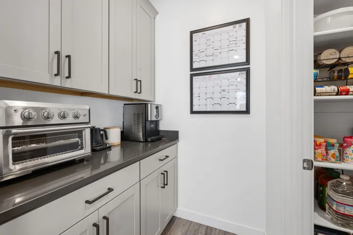 Light gray shaker cabinetry with dark hardware, dark countertop, and pantry with built-in shelving