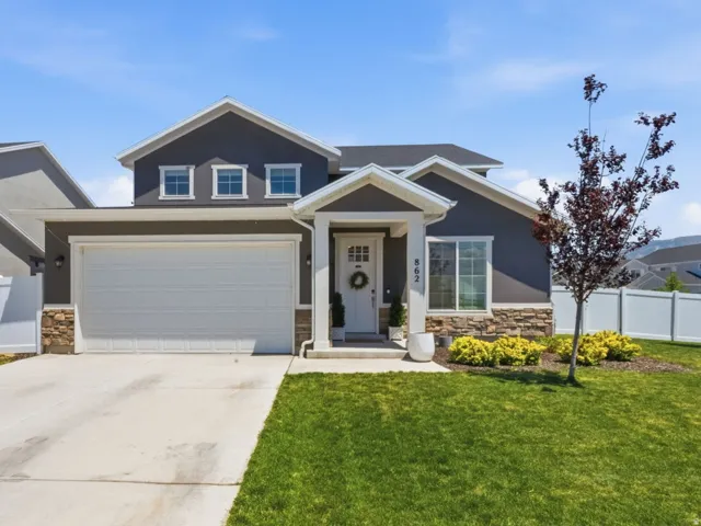 Modern residential exterior featuring a stone accent foundation, two-car garage, covered entry porch, and a manicured front lawn