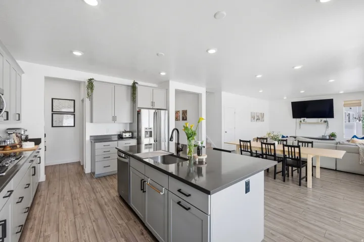Open-concept kitchen and dining area featuring wood-finish flooring, recessed lighting, and a large central island with a sink and dark countertop