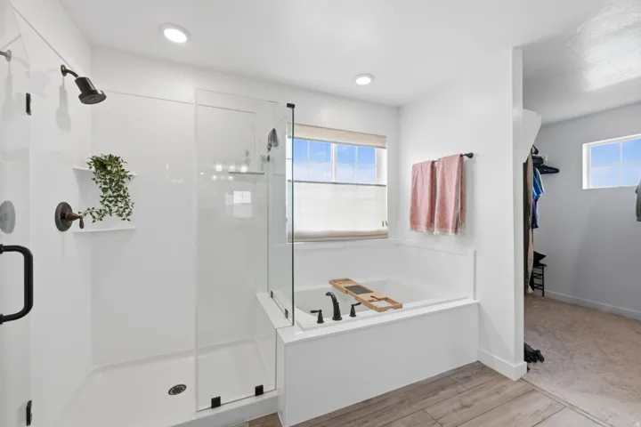 Bright bathroom featuring a glass-enclosed shower with bronze fixtures and a recessed shelf, a built-in soaking tub with dark fixtures, and wood-finish flooring