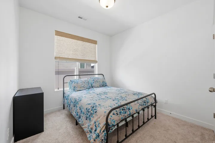 Bedroom featuring light-colored carpet, a window with a woven shade, and a flush-mount ceiling light fixture