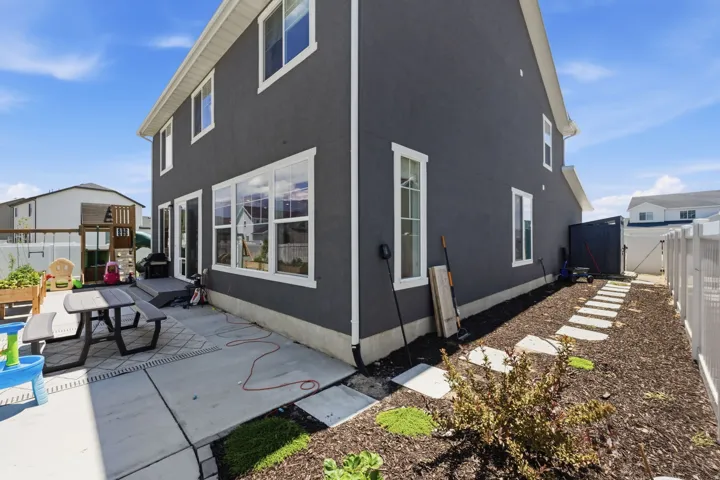 Exterior featuring dark stucco siding, white trim windows, and a concrete patio