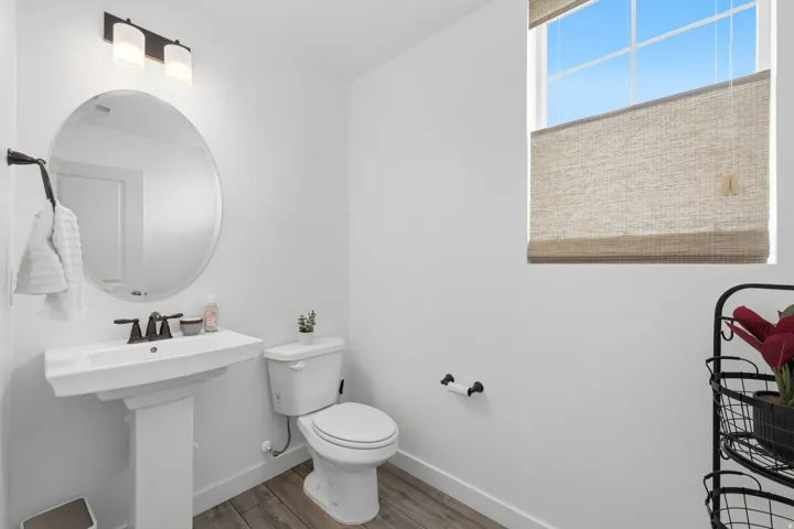 Bathroom featuring a pedestal sink, oval mirror, and wood-finish flooring