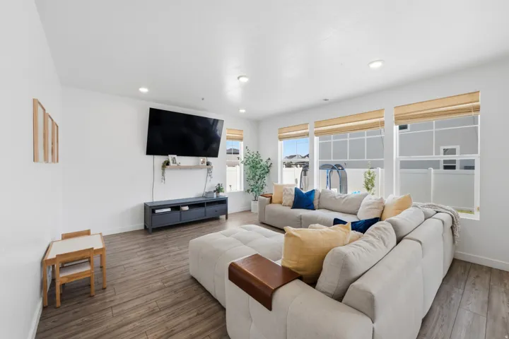 Spacious living area featuring wood-finish flooring, recessed lighting, and multiple windows with privacy blinds