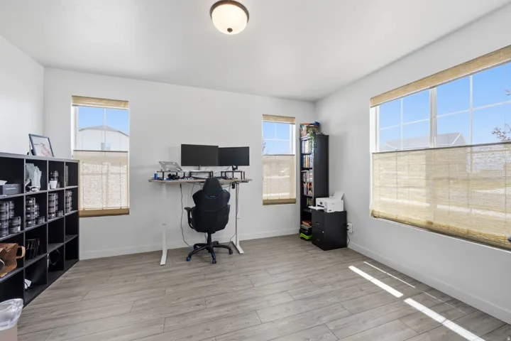 Spacious room featuring wood-finish flooring, multiple windows with blinds, a built-in overhead light fixture, and white wall finishes