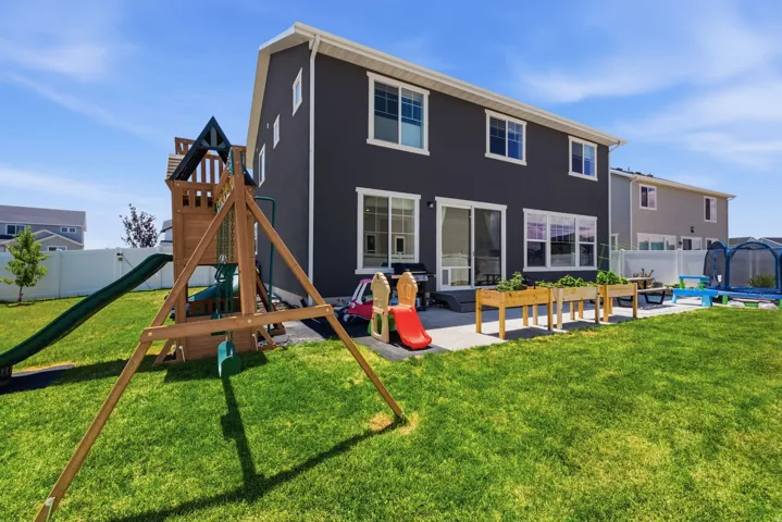 Spacious backyard featuring a large green lawn, a concrete patio, and three raised garden beds