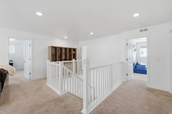 Upper-level landing with carpeted flooring, white balusters, recessed lighting, and a built-in wood-tone shelving unit