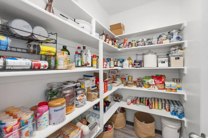 Walk-in pantry featuring extensive white shelving and wood-finish flooring