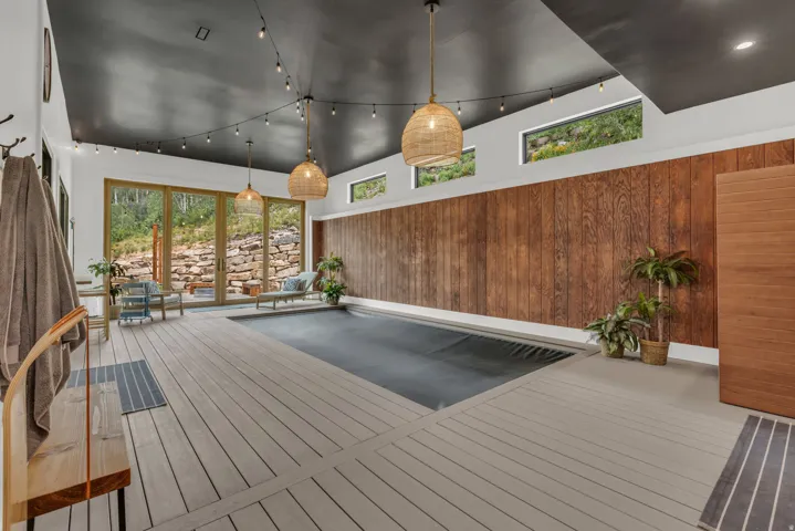 Indoor swimming pool area featuring wide plank deck flooring, a dark ceiling, and wood panel accent walls