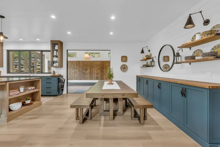 Open-concept interior featuring light wood-finish flooring, a dining area with a wood table and benches, and a custom built-in storage unit with blue cabinetry and wood-finish countertops