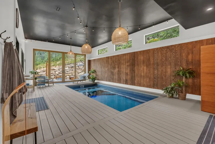 Indoor swimming pool with light-toned deck surround, framed by wood paneling and large glass doors