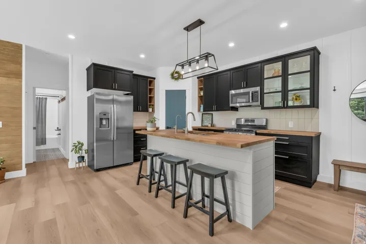 Kitchen featuring a central island with wood-finish countertop, stainless steel appliances, black cabinetry, white shiplap island paneling, and wood-finish flooring