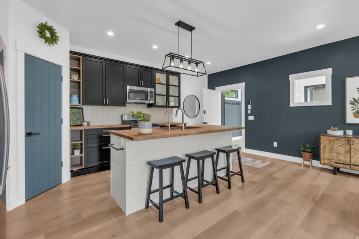 Contemporary kitchen featuring black cabinetry, light wood-finish countertops, stainless steel appliances, and a central island with bar seating