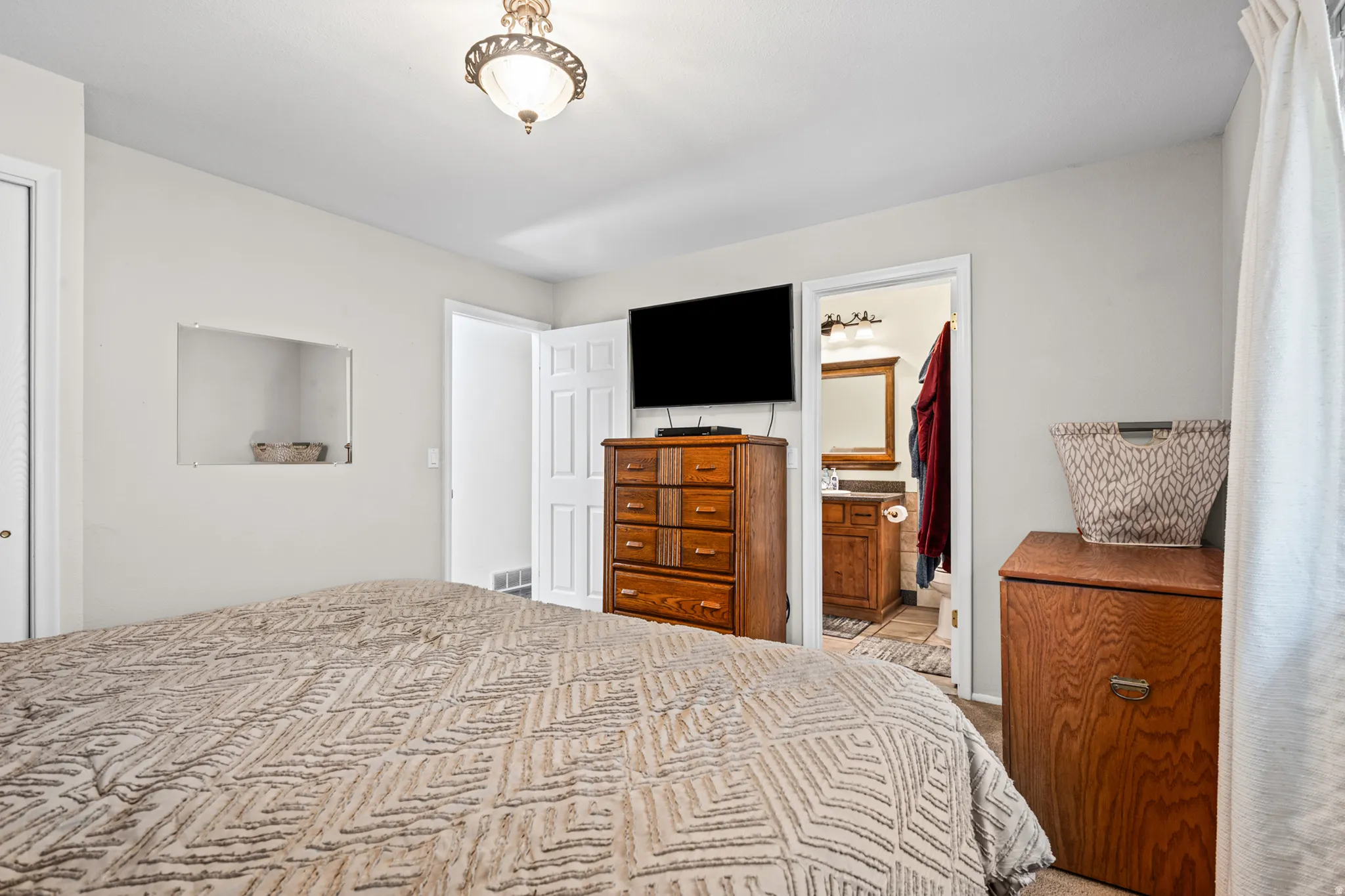 Bedroom with white walls and a ceiling-mounted light fixture, featuring a recessed wall niche, a paneled door, and wood-finish flooring