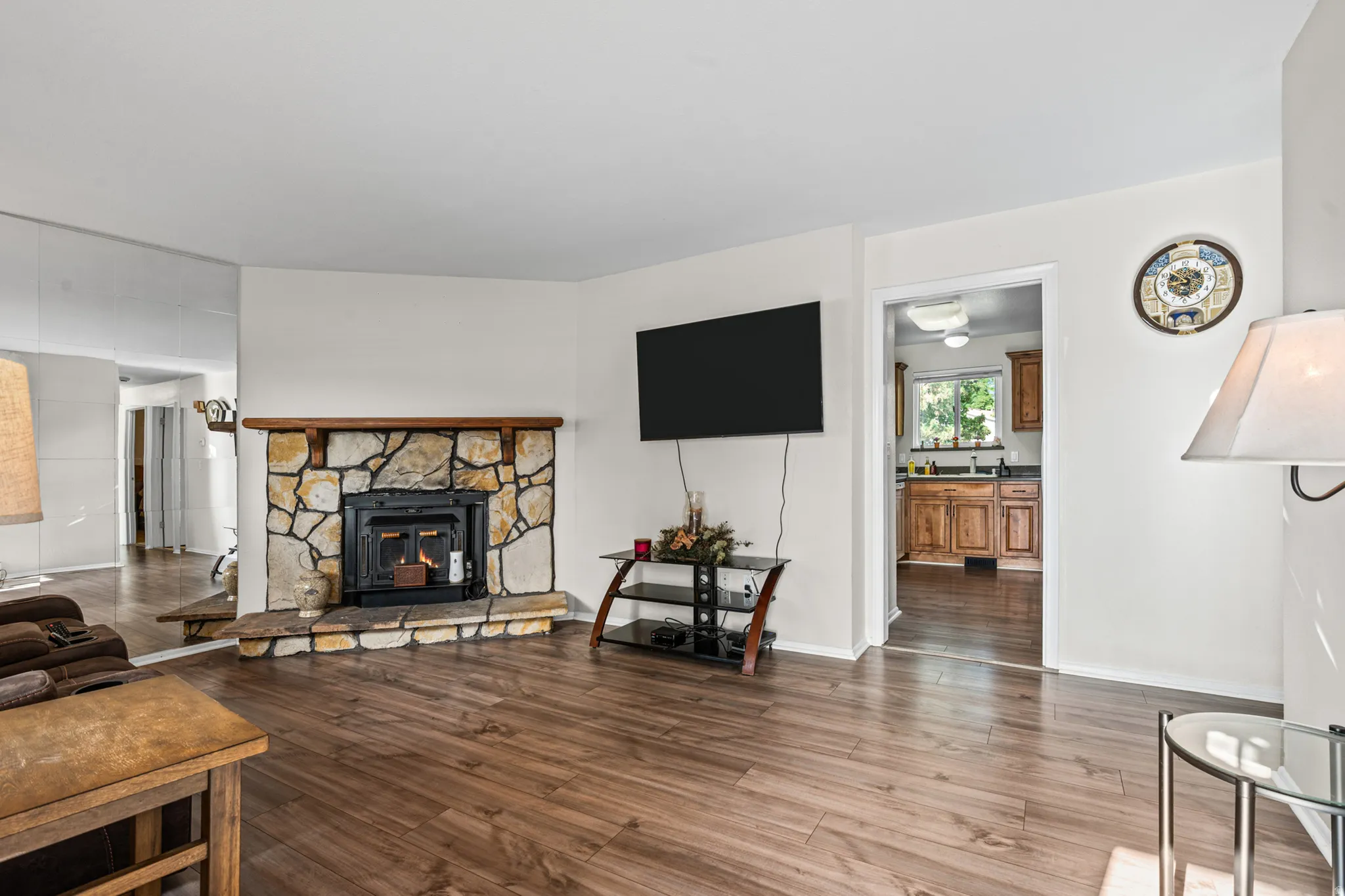 Living space featuring wood-finish flooring, a stone fireplace with a wood mantel, and white walls